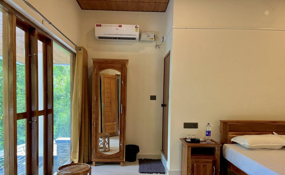 A bright bedroom at Olam with full-height balcony doors and a mirrored teak almirah