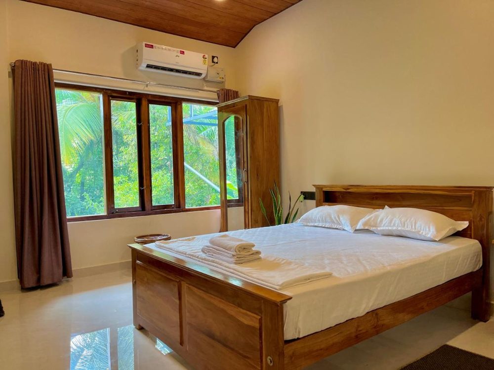 A bedroom at Olam with a panelled teak bed, folded towels and a window onto the garden