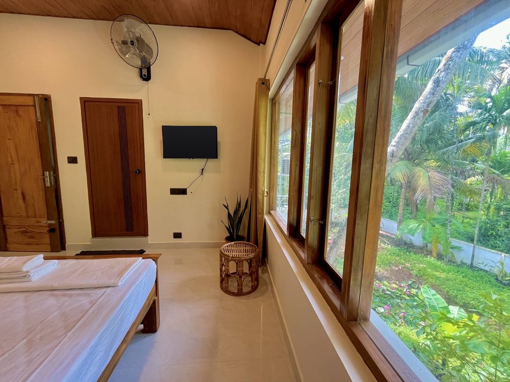 A bedroom at Olam with a corner window wall looking into the flowering garden and banana plants