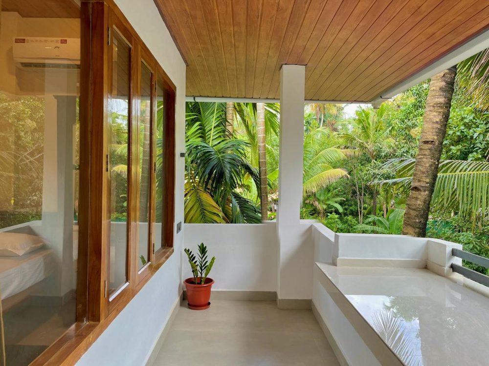 The verandah at Olam under deep eaves, white columns and a low parapet opening into the palm grove