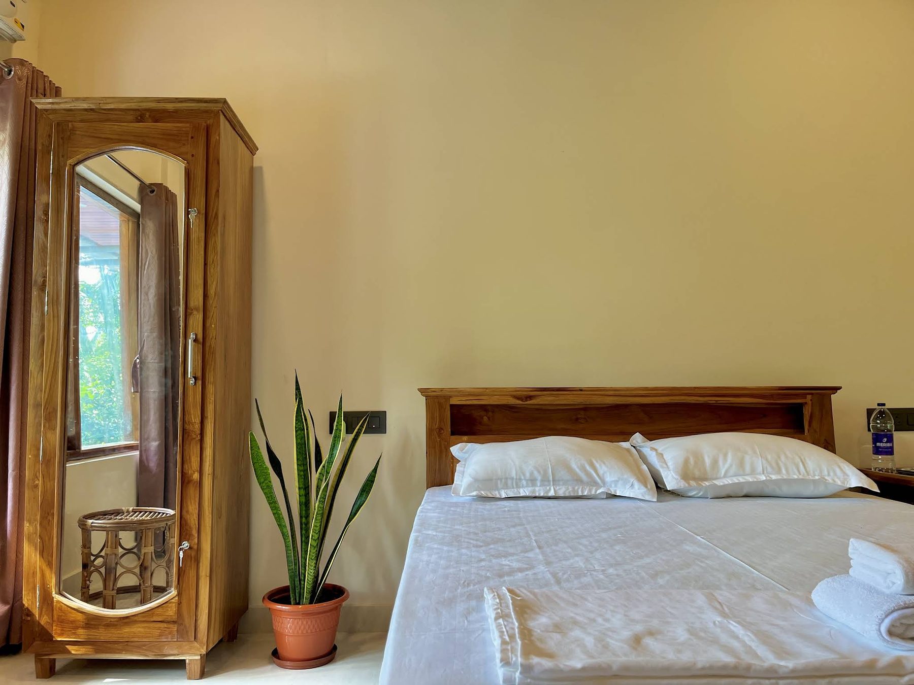 Teak bed with a panelled headboard and white pillows beside a mirror