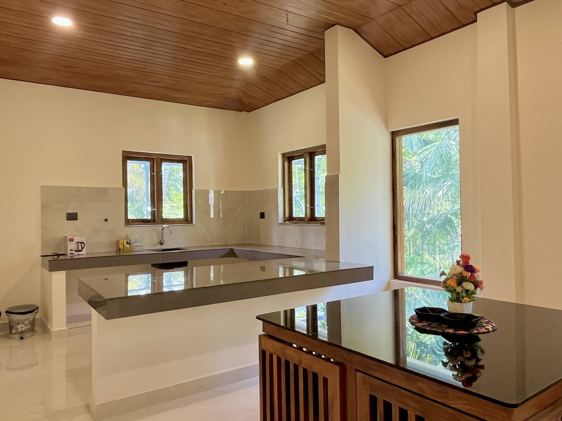 Open kitchen with a grey quartz L-shaped counter under teak-framed windows