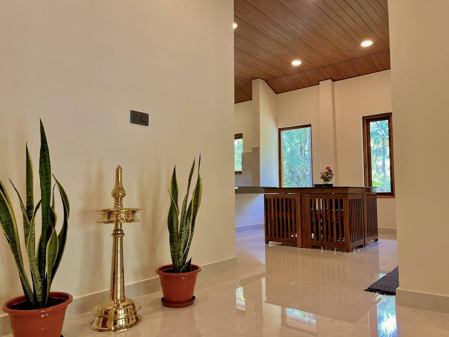 Entrance hall with a tall brass Kerala nilavilakku oil lamp between two snake plants