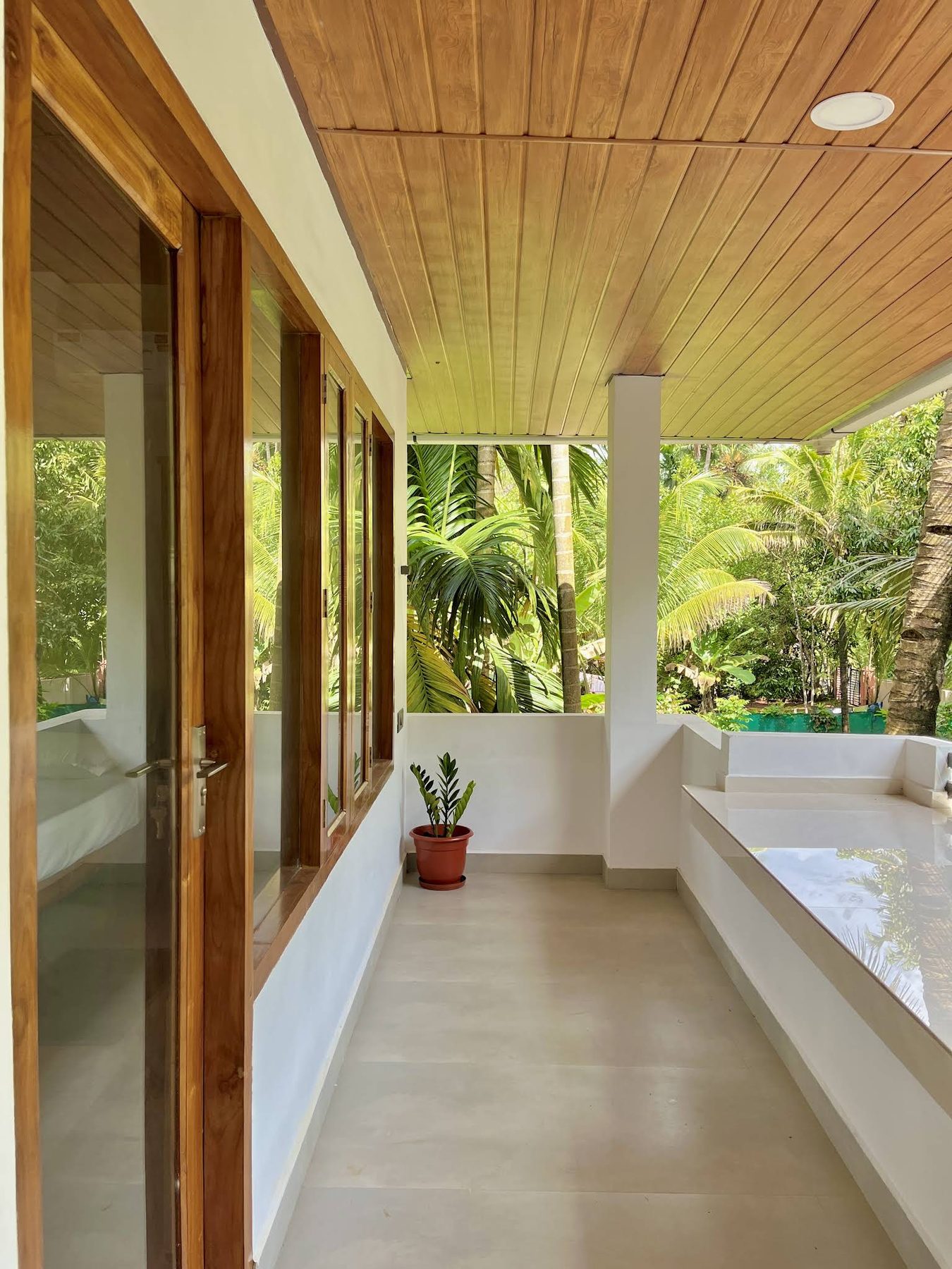 Verandah looking along white columns and a teak soffit toward dense green