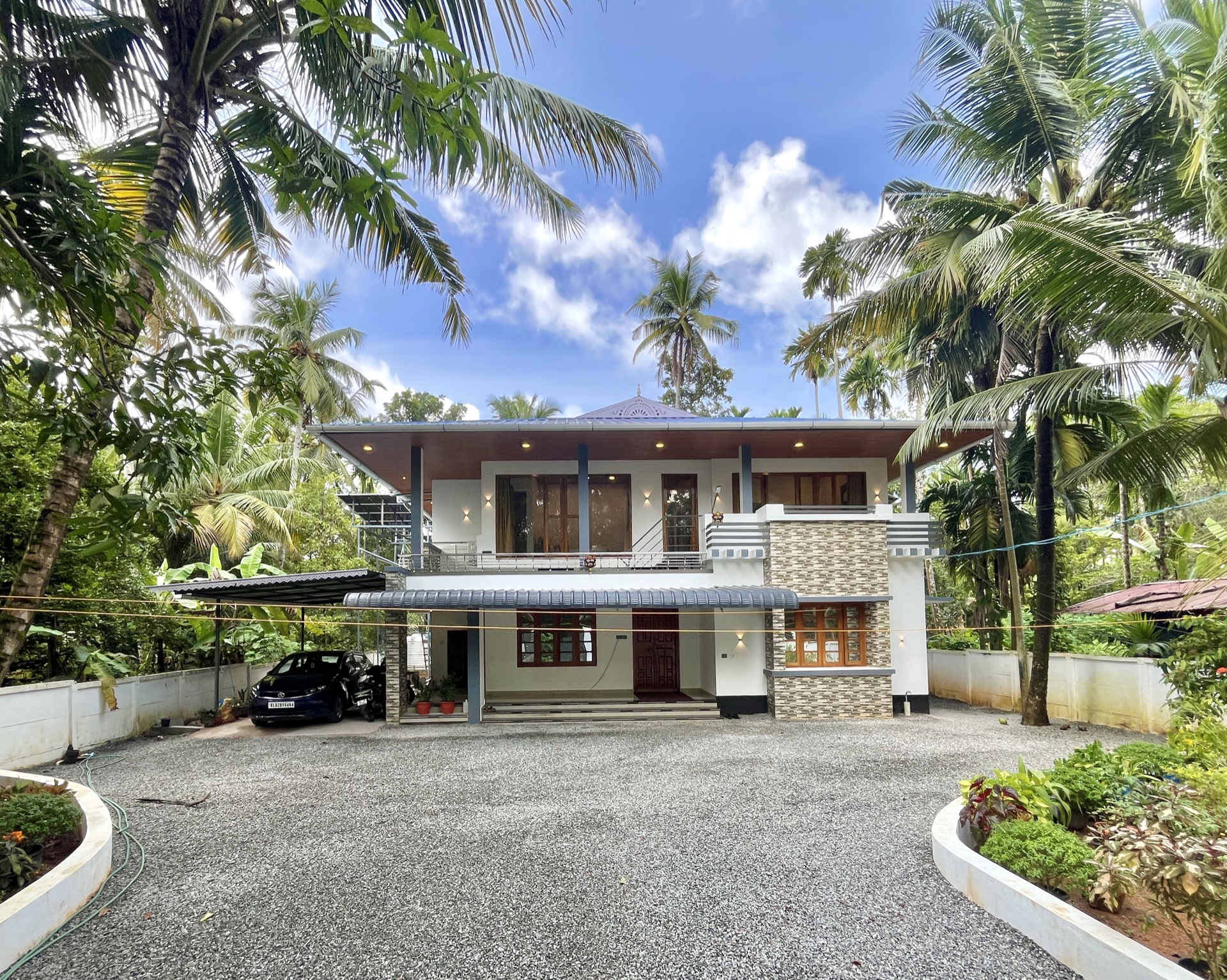 The house from the gravel yard, two storeys under a tiled roof, coconut palms on every side