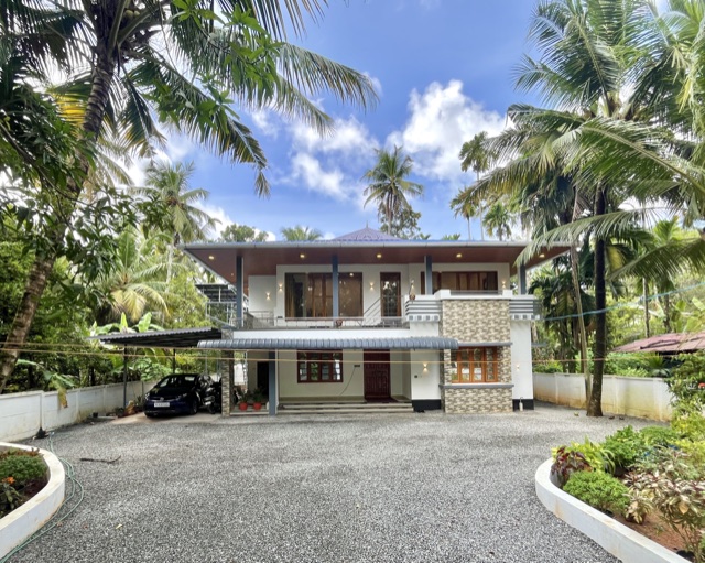 The house from the gravel yard, two storeys under a tiled roof, coconut palms on every side