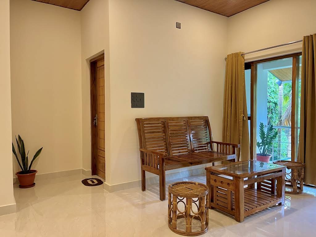 Living room with a teak slat settee, glass-topped table and rattan stools, curtains drawn back from a balcony door