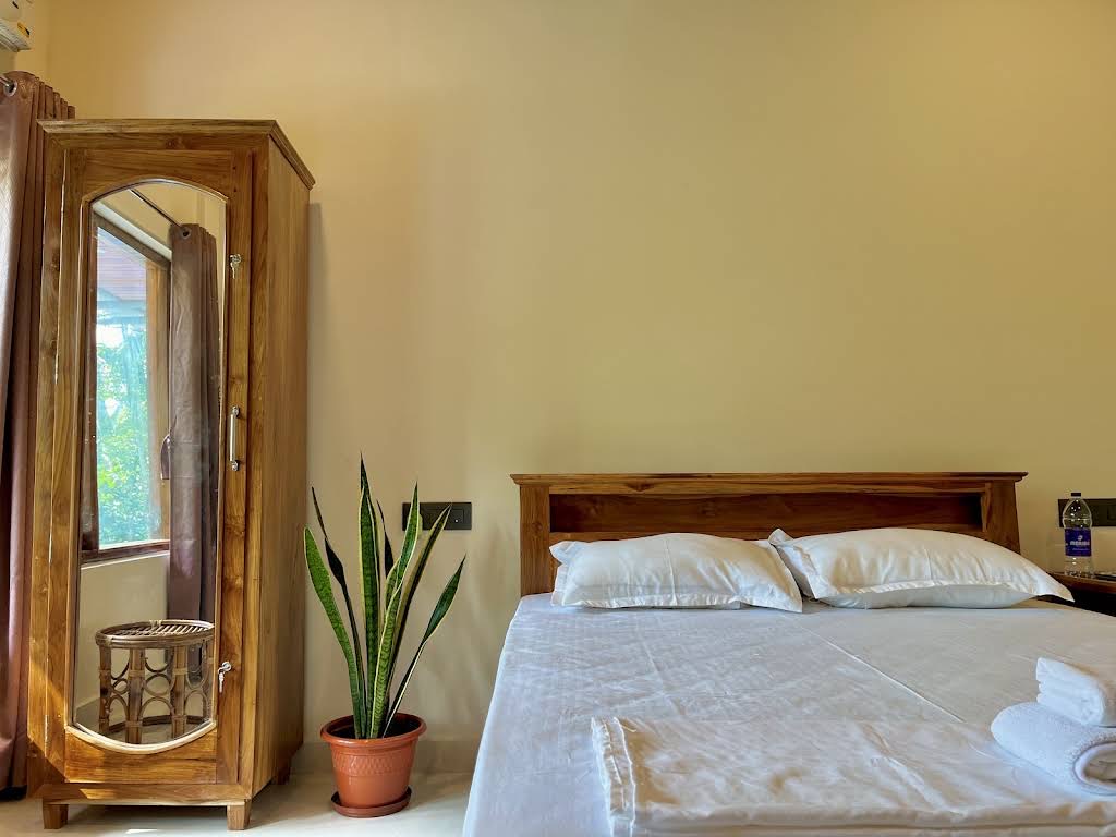 Queen bed made up in white with two pillows and a rolled towel, mirrored teak wardrobe reflecting the window