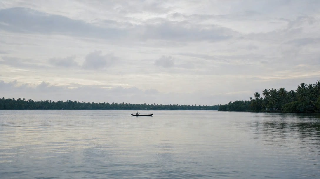 A lone canoe far out on the flat grey evening water of Ashtamudi Lake